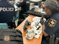 Police woman with firearm and cleaning cloth sitting at table wearing gloves