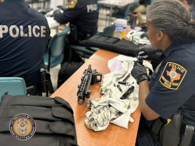 Police woman with firearm and cleaning cloth sitting at table wearing gloves