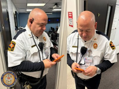 Man wearing a security uniform looking at mobile phone while wearing radio earpiece