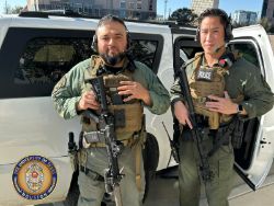 Two male police officers posing outdoors wearing special response team uniforms and holding police equipment